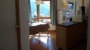 Zona pranzo con tavolo e sedie, un bancone cucina con elettrodomestici e una finestra con tende.