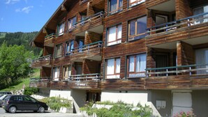 Un edificio in legno su più piani con balconi, un'area di parcheggio e montagne sullo sfondo.