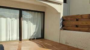 Un patio iluminado por el sol con puerta corrediza de vidrio, piso de concreto y pared de madera.