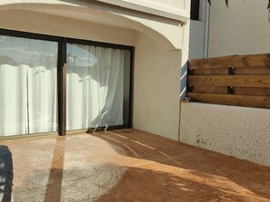Un patio iluminado por el sol con puerta corrediza de vidrio, piso de concreto y pared de madera.