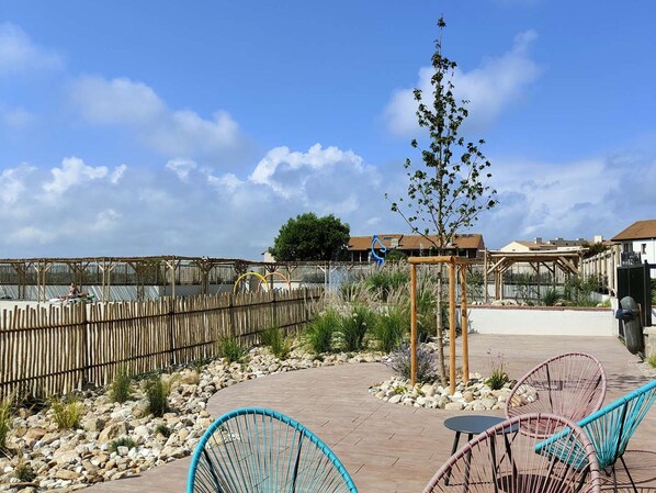 An outdoor patio area with wicker chairs, a small tree, and a wooden pergola.