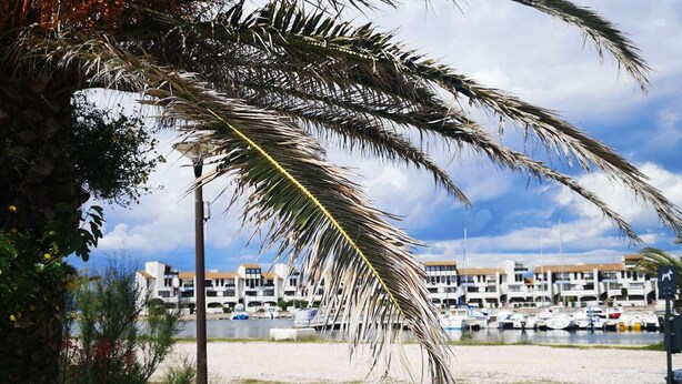 Un puerto costero con barcos, una playa de arena y una hilera de edificios al fondo.