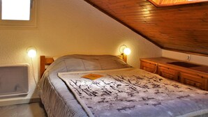 Un dormitorio con techo inclinado, una cama con manta estampada, lámparas de noche y una ventana.