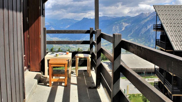 Un balcón de madera con una mesa y sillas, con vistas a un paisaje montañoso.