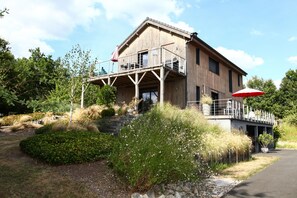 A wooden building with a balcony, surrounded by landscaped gardens and a paved path.