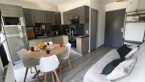 Eine kleine Küche mit modernen Geräten, ein Essbereich mit rundem Tisch und Stühlen sowie ein Bett mit Kissen.