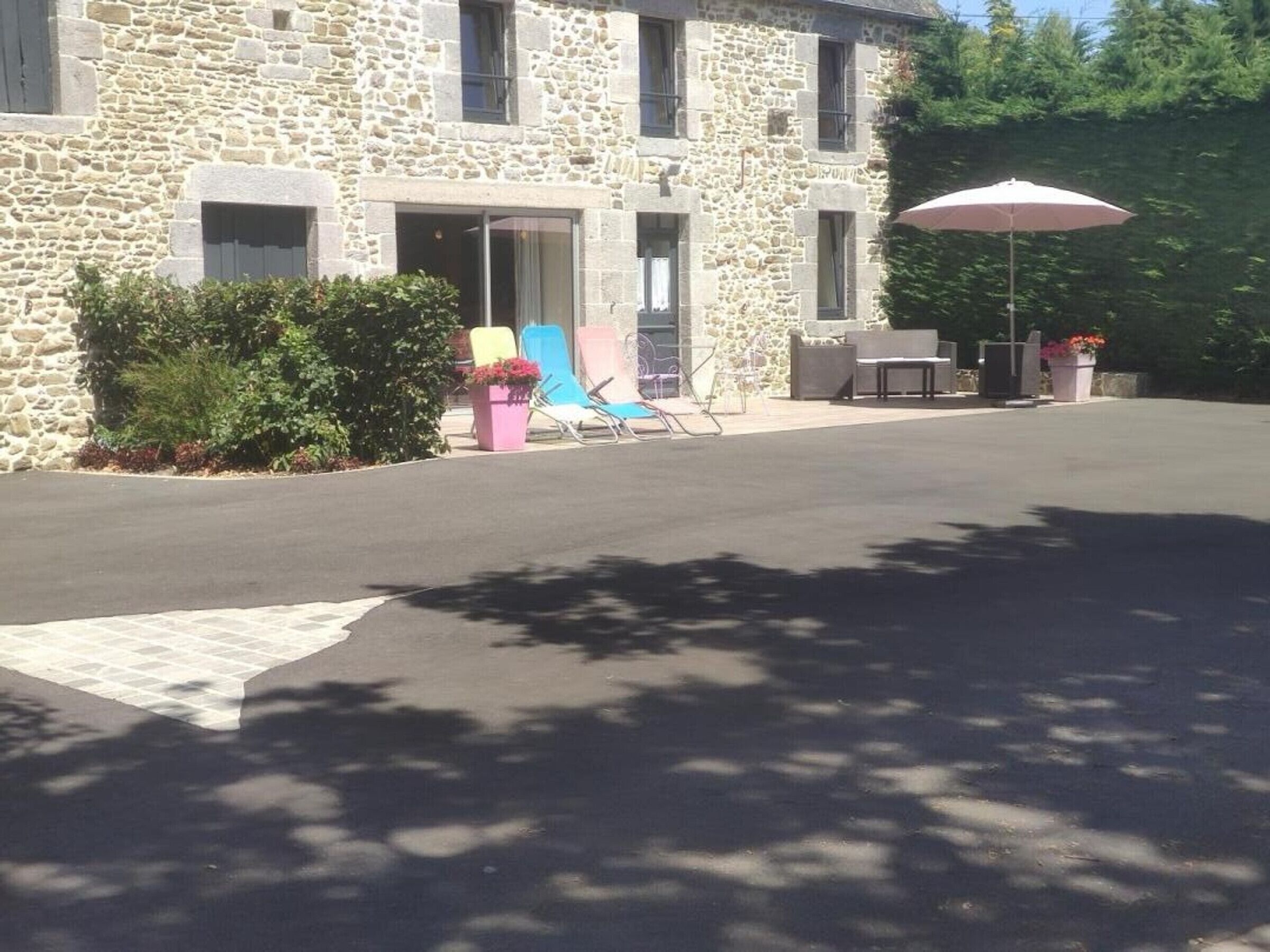 Un bâtiment en pierre avec une allée pavée, un espace extérieur aménagé pour s’asseoir et un grand parasol.