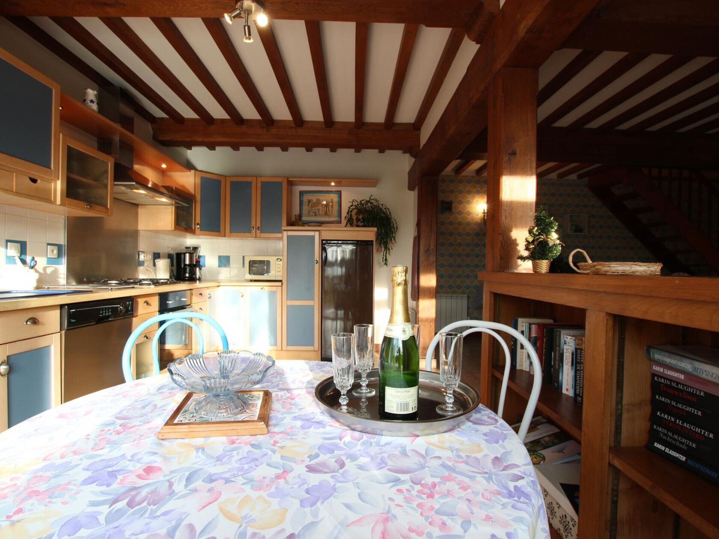 Uma cozinha acolhedora com vigas de madeira, uma mesa de jantar posta com toalha de mesa florida e uma garrafa de champanhe.