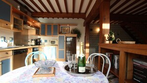 A cozy kitchen with wooden beams, a dining table set with a floral tablecloth, and a bottle of champagne. - Charming house in Lingreville near beach, for 5 pers, with Wi-Fi and pets allowed (Lingreville)