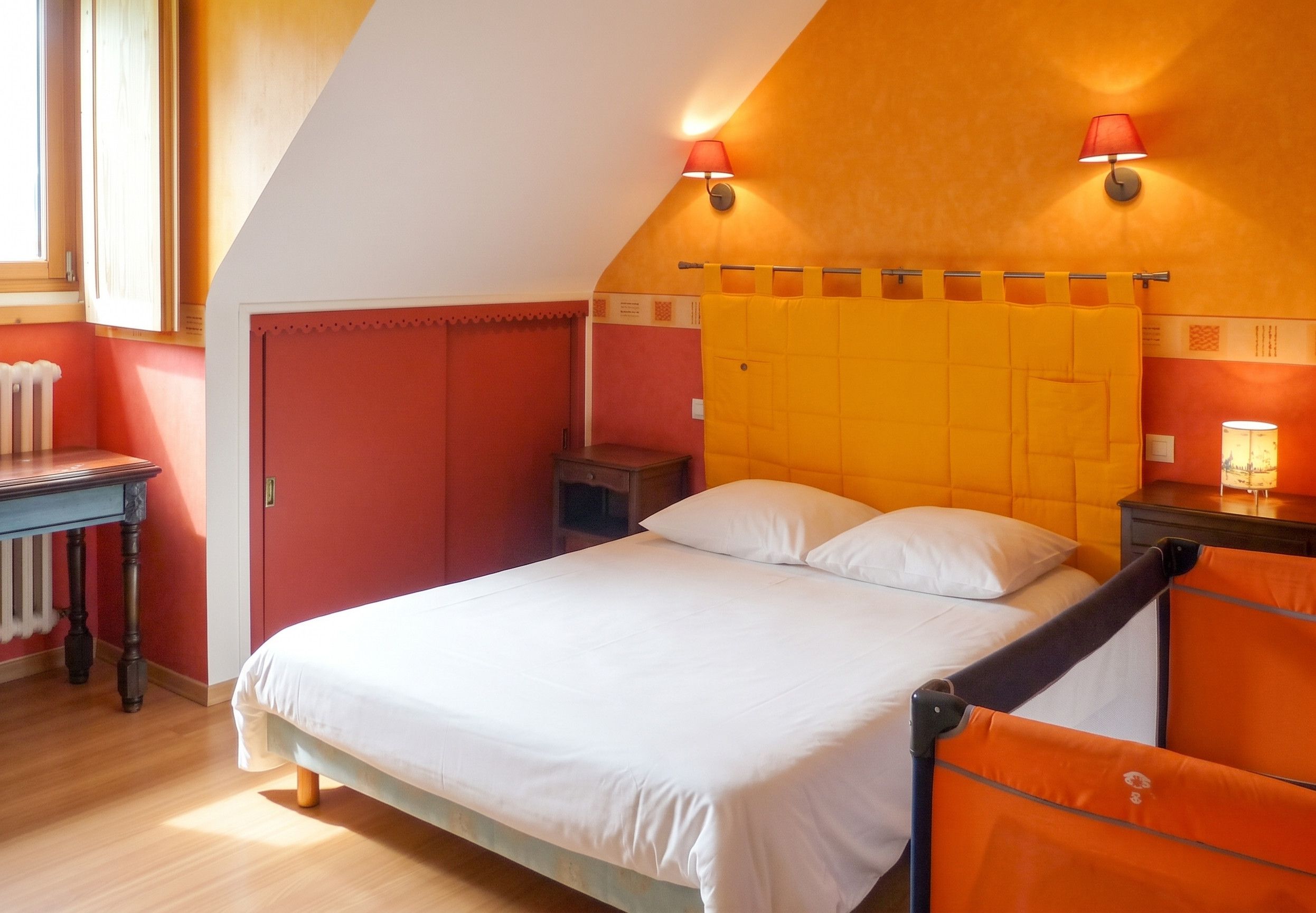 A bedroom with a bed, a nightstand, a chair, a radiator, and a window.