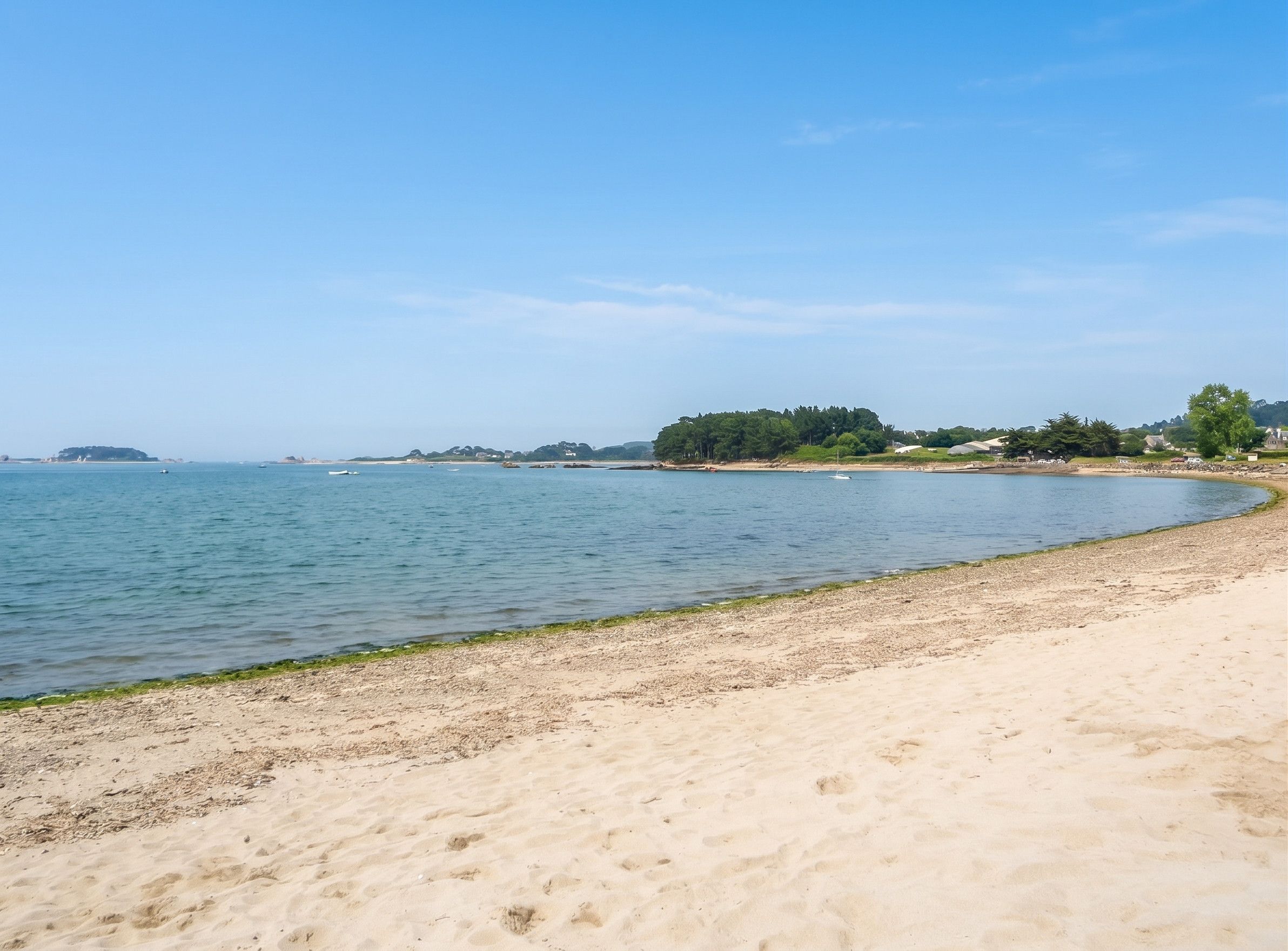 Een zandstrand met kalm water, een heldere lucht en landschappen in de verte.