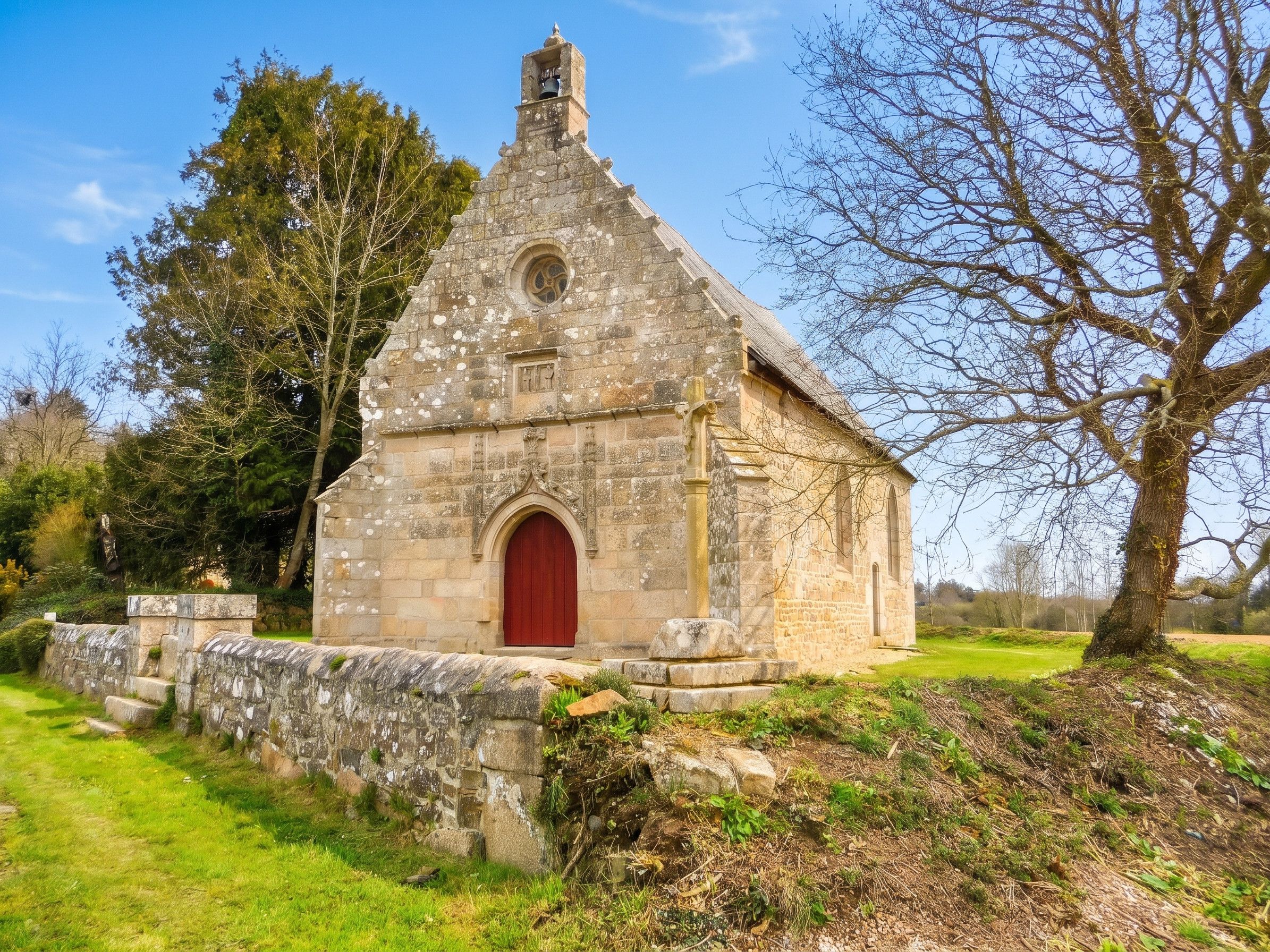 A small stone church with a red door, surrounded by grass and trees.