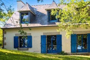 Uma casa de dois andares com telhado triangular, persianas azuis e fachada de tijolos.