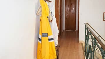Un couloir doté d’un plancher en bois, un porte-manteau avec des vêtements jaunes et blancs, et une porte en bois au fond.