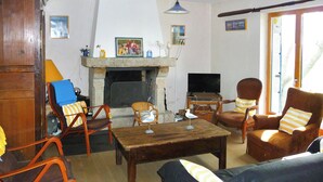 A living room with a fireplace, wooden furniture, a television, and a large window. - Homerez - House in Plougrescant. (Plougrescant)