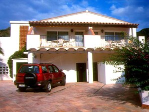 A two-story house with a tiled driveway and a red car parked in front.