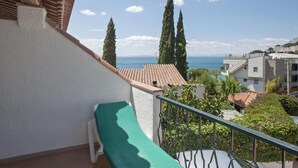 Ein Balkon mit einem grünen Stuhl, der auf eine Küstenlandschaft mit Gebäuden und hohen Bäumen blickt.