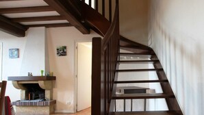 A wooden staircase in a room with a fireplace and a door leading to another area.