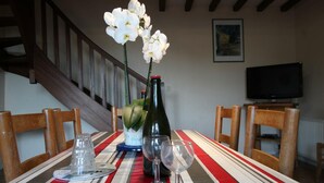 A dining table with a striped tablecloth, a bottle of wine, and two wine glasses. There is a staircase in the background and a television on a stand.