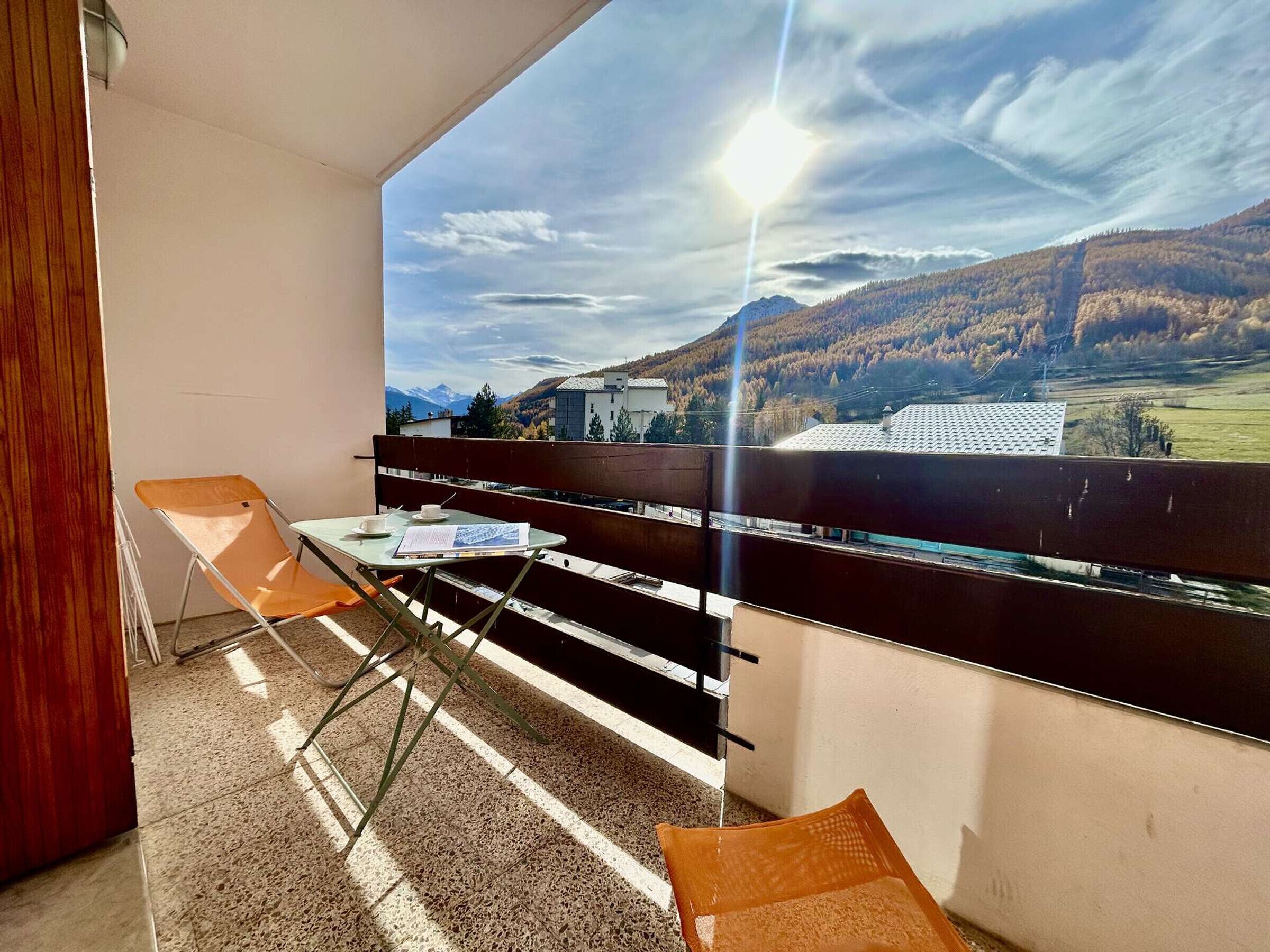 A balcony with a table, chairs, and a view of a mountainous landscape.