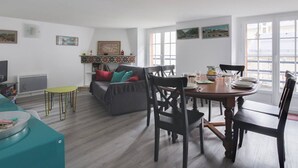 A spacious living room with a dining area, a grey sofa with colorful cushions, a television, and a bookshelf. - Duplex 3-Room 6-Person with Balconies, Near Ski Lifts and Amenities, Heart of Cauterets (Cauterets)