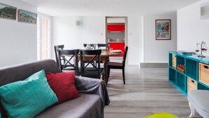 A modern living room with a grey sofa, a dining table with chairs, a kitchen area with red cabinets, and a blue shelving unit. - Duplex 3-Room 6-Person with Balconies, Near Ski Lifts and Amenities, Heart of Cauterets (Cauterets)