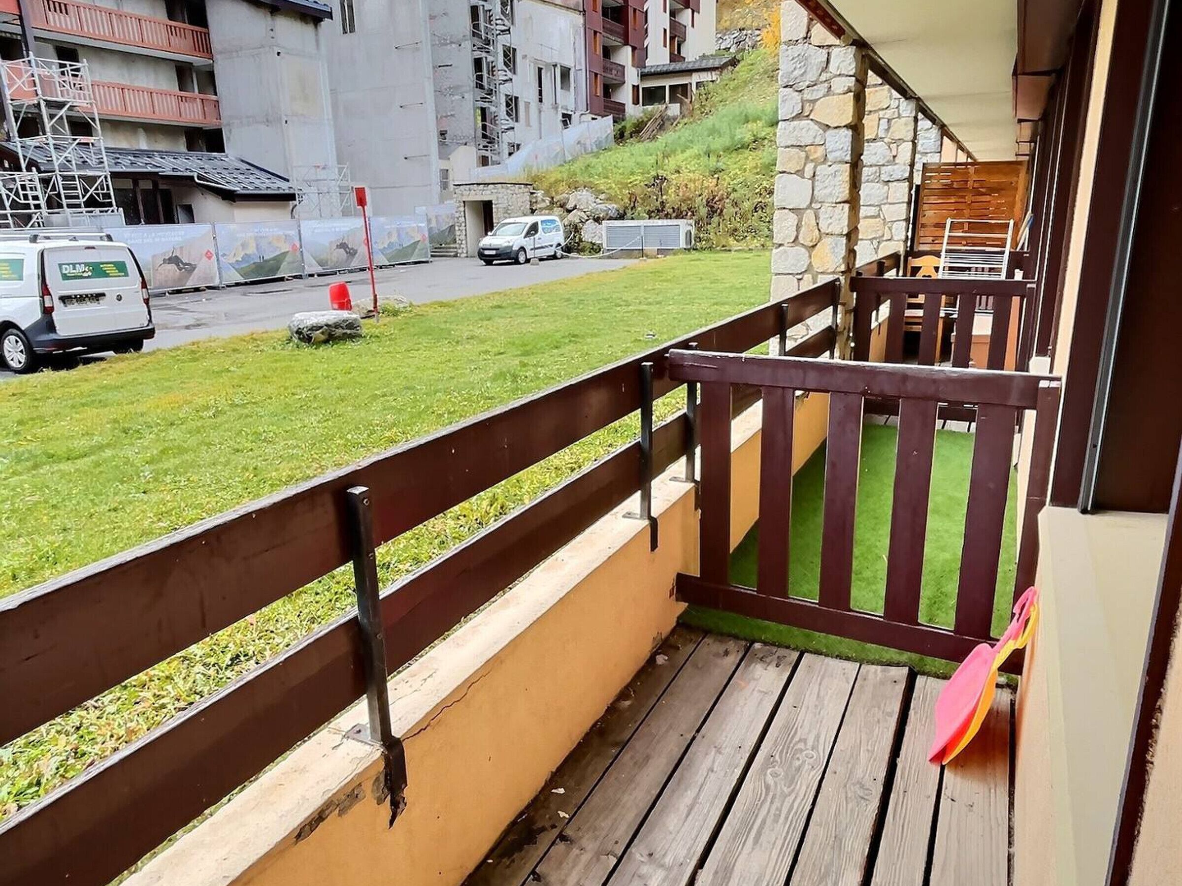 Ein Balkon mit Holzgeländer, der auf eine Rasenfläche und eine Straße mit geparkten Autos blickt.