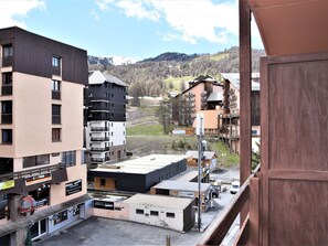 A multi-story building with balconies, a parking area, and a view of a mountainous landscape.