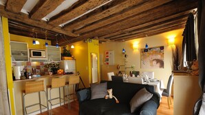 Ein gemütliches Wohnzimmer mit einem dunkelblauen Sofa, einem kleinen Tisch und einer Küchenzeile mit Mikrowelle und Barhocker.