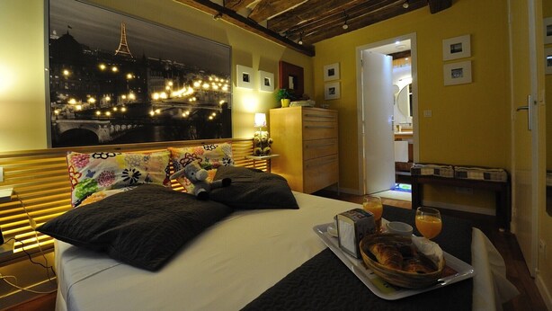 Ein Hotelzimmer mit Bett, einem Nachtblicksplakat, einem Schminktisch und einem Frühstücksbrettchen.