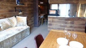 A cozy room with a wooden wall, a sofa, a dining table with wine glasses, and a kitchen area with a microwave.