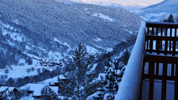 A mountain landscape with snow-covered trees and a wooden fence.