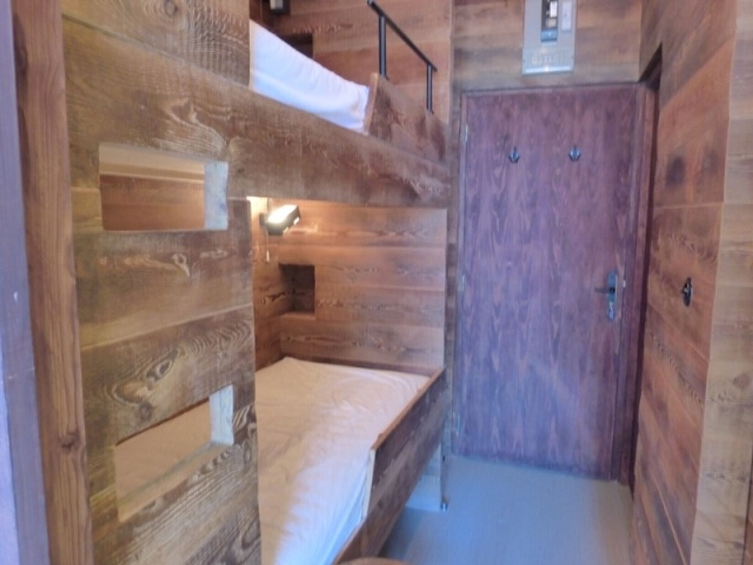 A wooden cabin with bunk beds, a small window, and a door.