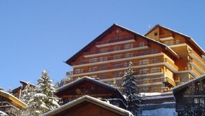 A multi-story wooden building with balconies, likely a hotel or lodge, surrounded by snow-covered trees.