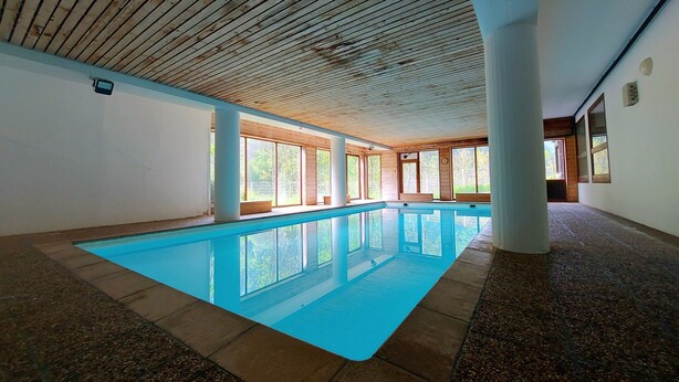 Ein Hallenbad mit klarem, blauen Wasser, Holzbalkendecke und großen Fenstern.