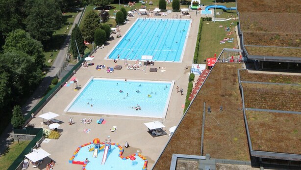 A swimming pool complex with multiple pools and a children's play area, surrounded by a mountainous landscape.