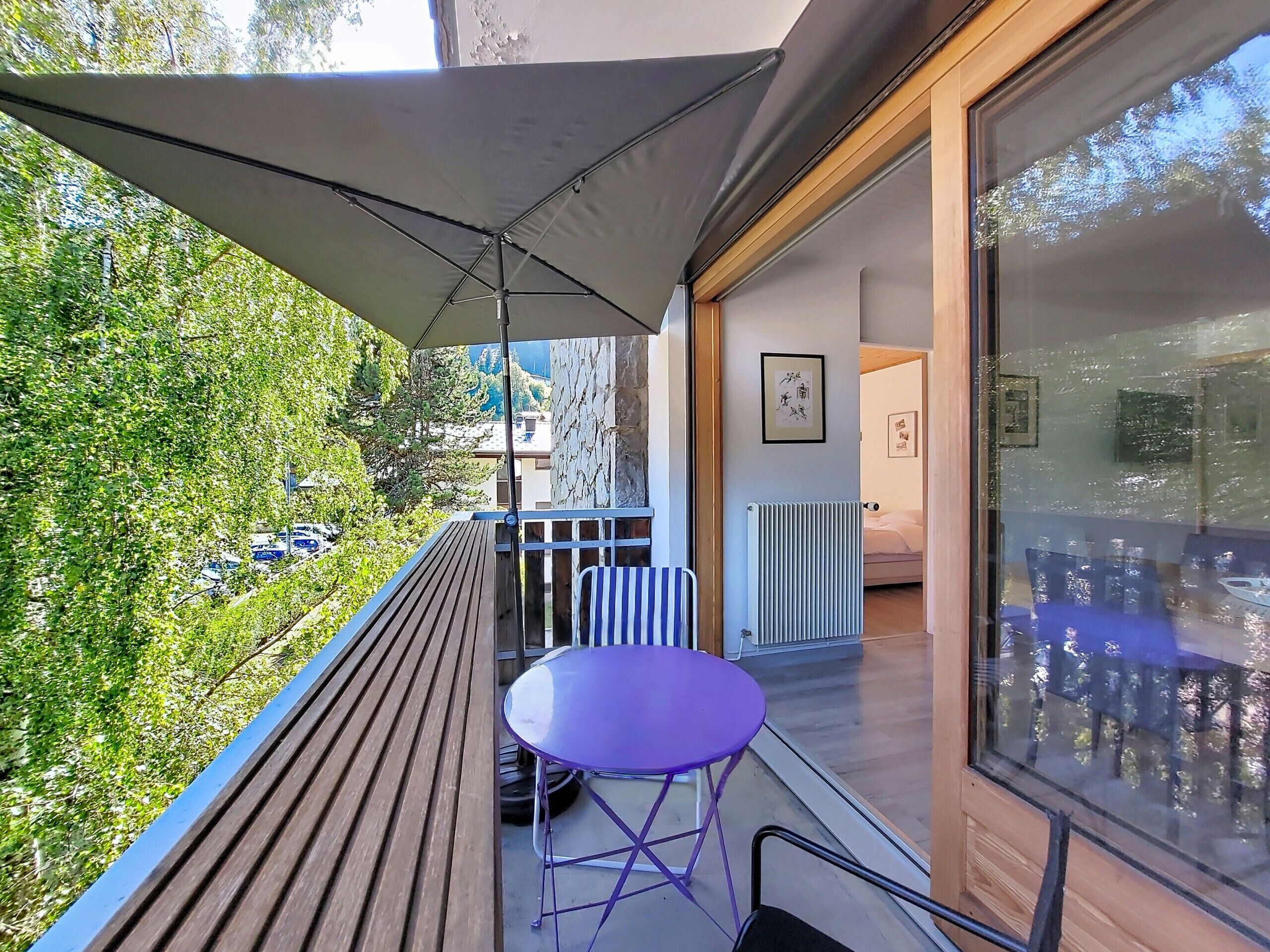 Un balcon avec une table et des chaises, une vue sur un jardin et l’entrée d’un immeuble.