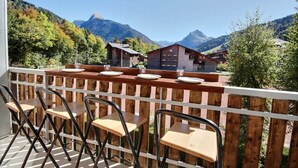 A balcony with wooden railings, a table set with plates and glasses, and mountain views in the background.