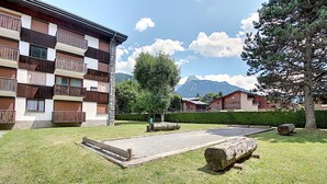 A courtyard with a shuffleboard table, a stone building with wooden balconies, and a mountain in the background.