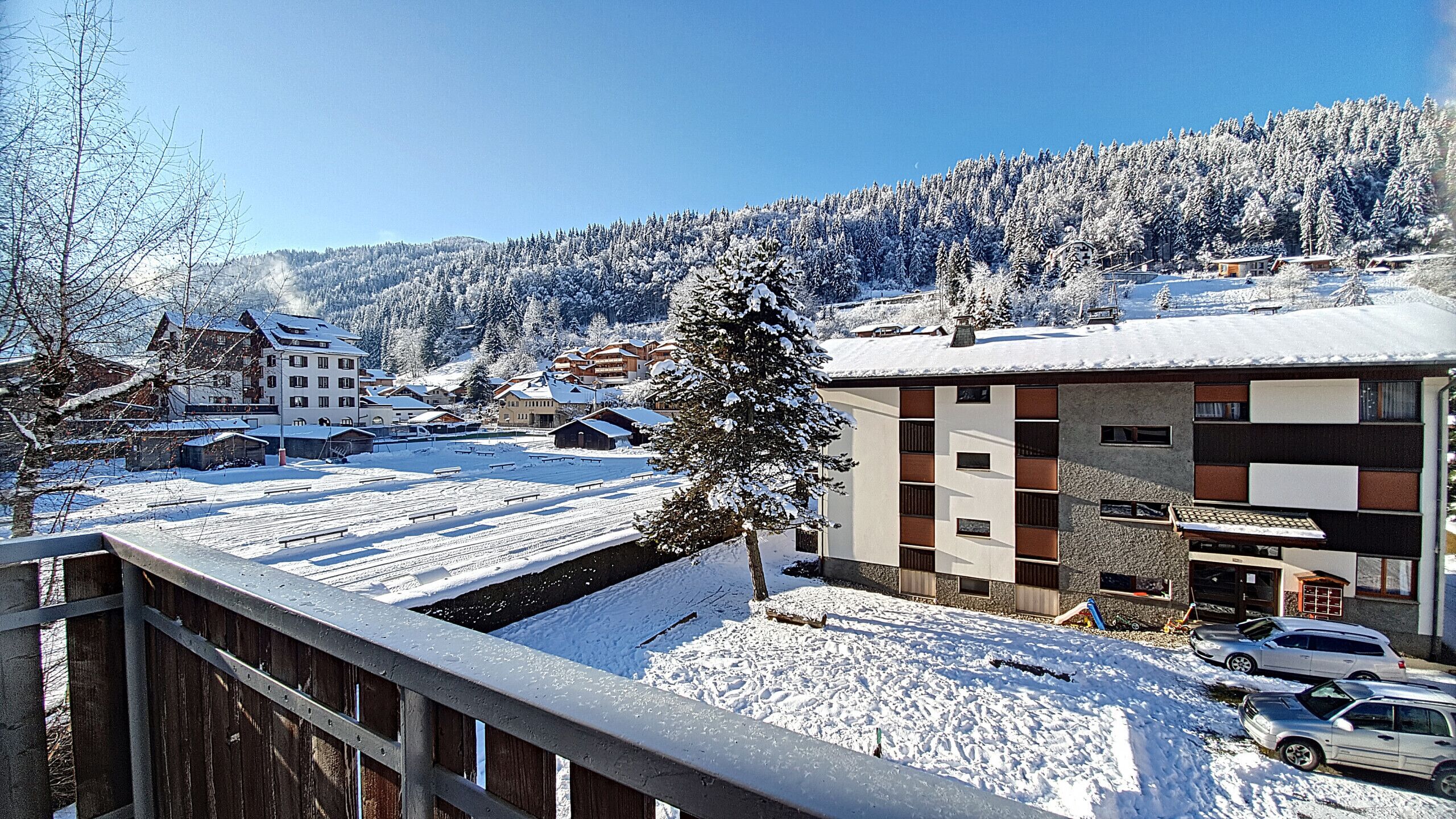 A snow-covered building with a modern design, surrounded by a snowy landscape and a forested hill.