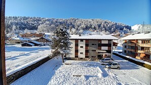 A snow-covered building with a modern design, surrounded by a snowy landscape and a forested hill in the background.