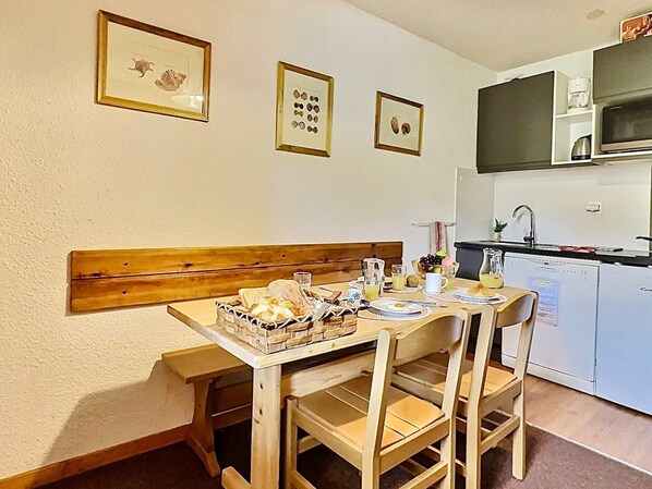 A dining area with a wooden bench and table, a kitchen with a microwave and sink, and framed pictures on the wall.
