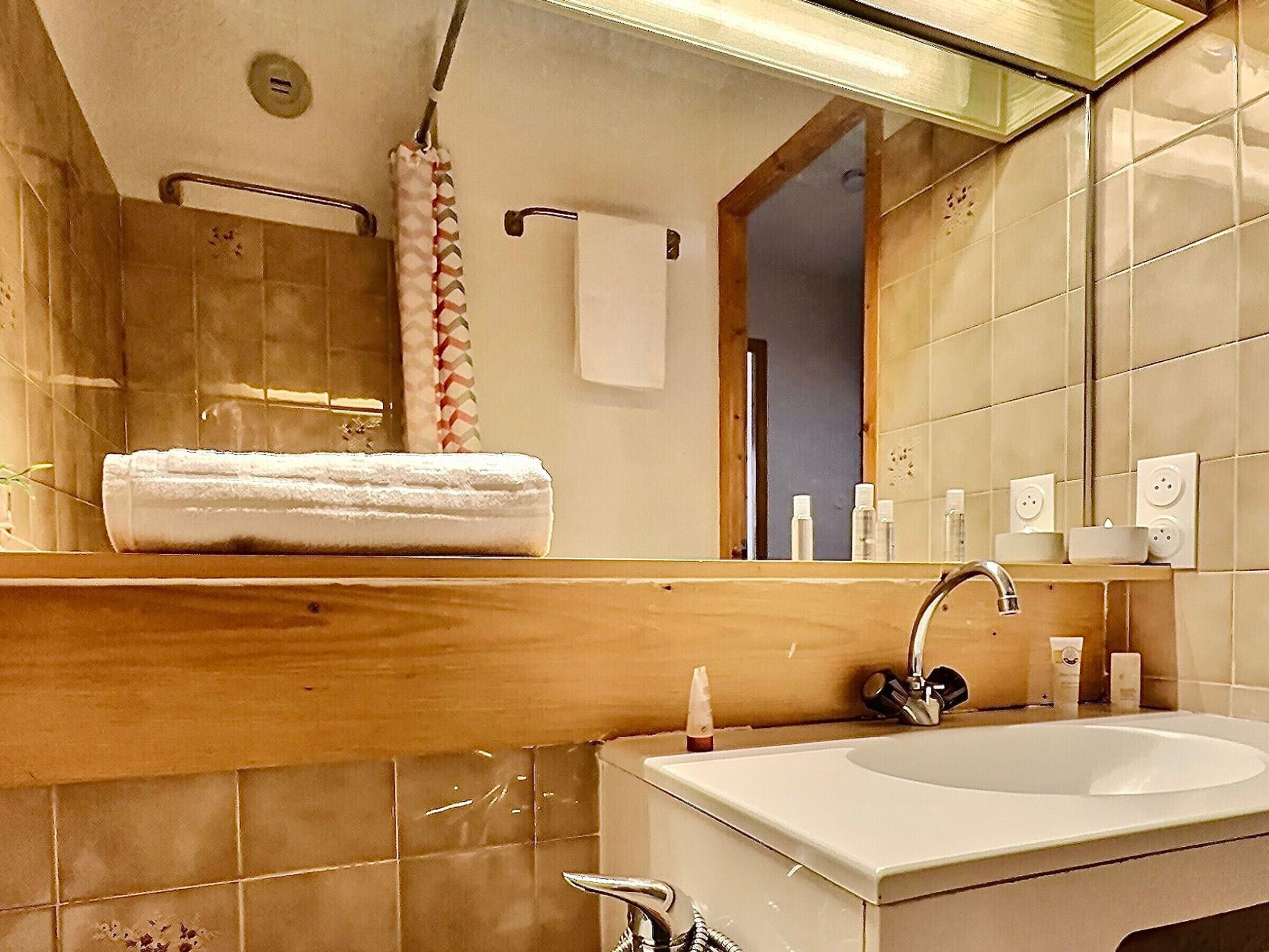 A bathroom with a wooden vanity, a sink, a mirror, and a shower area.