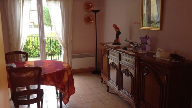 A dining area with a table and chairs, a cabinet with decorative items, and a view through a window.