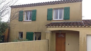 A two-story building with a beige facade, green shutters, and a tiled roof.