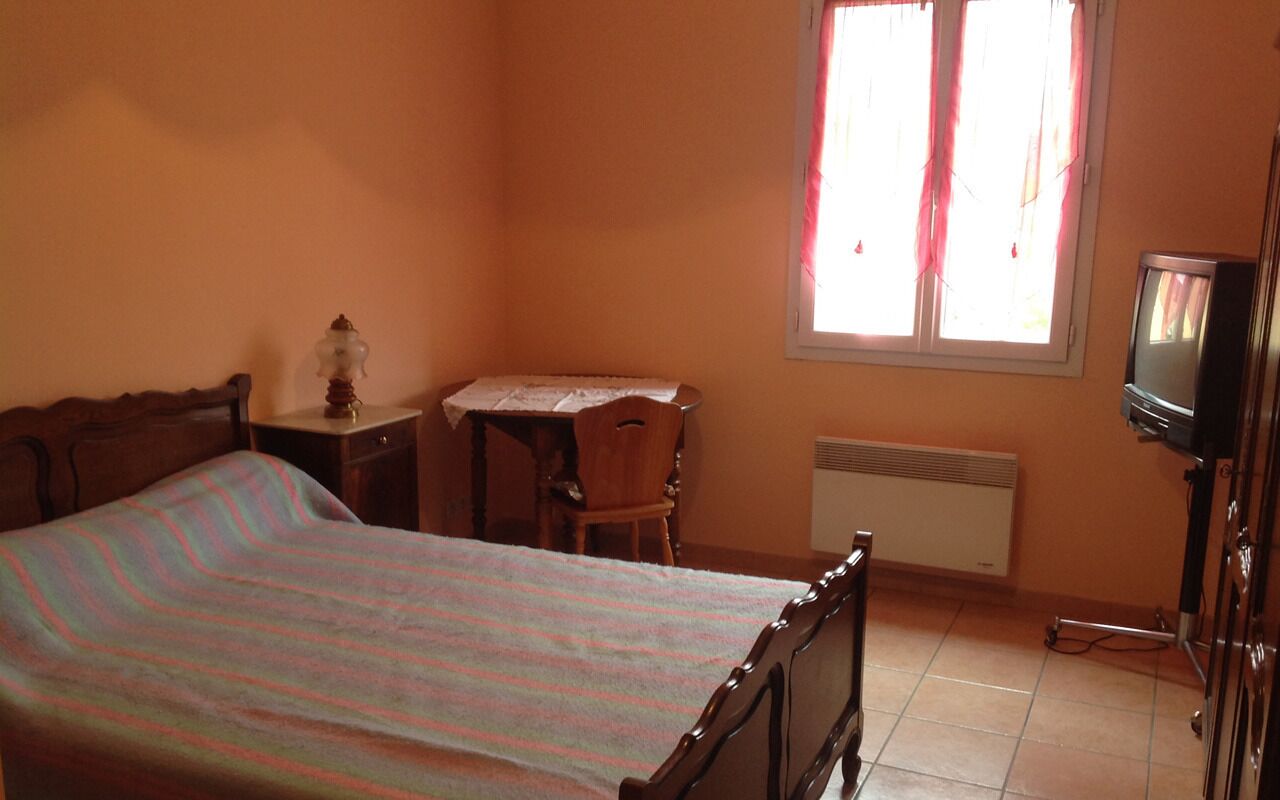 A bedroom with a bed, a small table, a chair, a radiator, and a television.