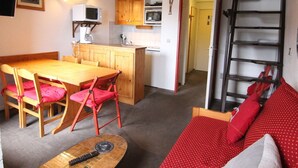 A compact living space with a dining area, kitchenette, and a staircase. - 2P-Mezzanine Apartment for 6 in Alpe d'Huez (Huez)