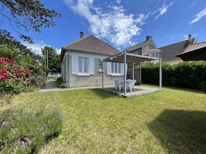 A house with a covered patio, a lawn, and a garden with flowers.