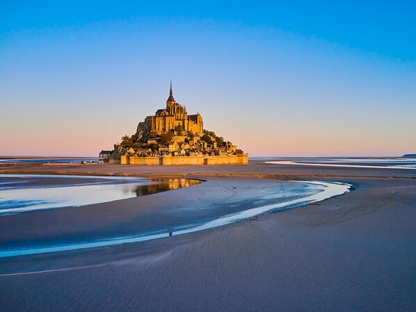 A cathedral-like structure with a prominent spire, situated on a sandy beach with a calm water body in the foreground.
