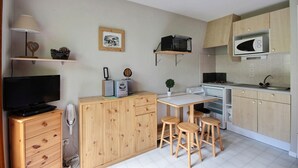 A compact kitchen with wooden cabinets, a microwave, a stove, and a small dining area with stools. - STUDIO APARTMENT IN THE HEART OF THE SKI RESORT - SAINT JEAN D'AULPS SKI RESORT -4 PEOPLE - PANORAMIQUE 26 (Saint-Jean-d´Aulps)